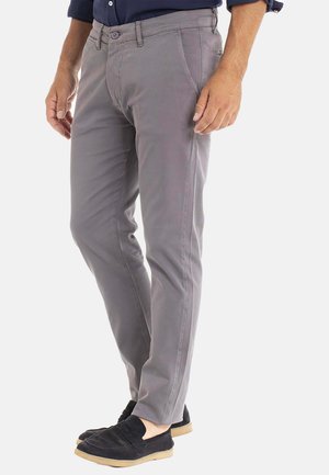 Pantalon gris en tissu léger, avec une coupe slim, des passants de ceinture et des poches avant. Porté avec des mocassins noirs.