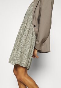 Vestido floral verde claro con falda acampanada, combinado con un blazer topo. El vestido tiene pequeños puntos negros y marinos.