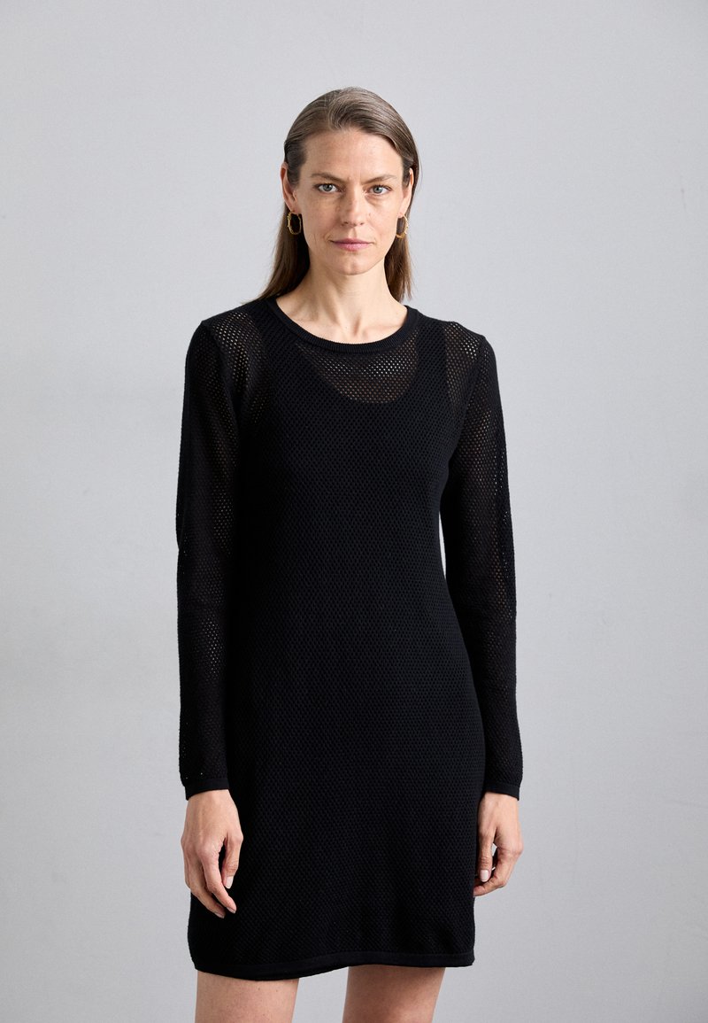 Abito in maglia nera con maniche lunghe, caratterizzato da un design a trama aperta e testurizzata. Collo rotondo e taglio dritto, che cade sopra il ginocchio.