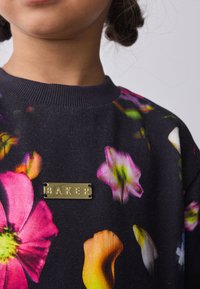 Must musta pusa, millel on erkroosad, oranžid ja valged lillemustrid. Kaelusel on kinnitatud kuldne metallist silt "BAKER".