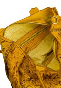 Yellow leather handbag with embossed floral design, featuring a zippered pocket and fabric lining, showcasing a distinctive shape and texture.