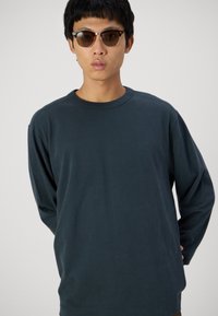 Dark blue long-sleeve t-shirt in soft cotton with a crew neckline. Accompanied by brown-tinted sunglasses with a tortoiseshell frame.