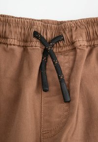 Brązowe szorty z elastycznym paskiem w talii, z czarnym sznurkiem i pomarańczowymi akcentami, o miękkiej teksturze materiału oraz przeszytych detalach kieszeni.