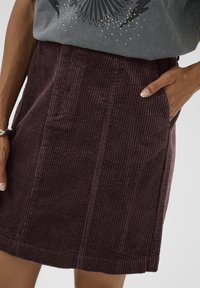 Jupe en velours côtelé violet présentant des côtes verticales, des poches latérales et une coupe droite. Le tissu a une texture douce et une finition lisse.