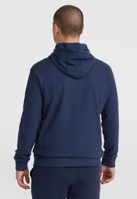 Hoodie bleu marine avec une coupe décontractée, texture douce et capuche avec cordon de serrage. Il présente des poignets et un ourlet côtelés, ainsi que des coutures visibles.