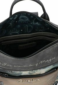 Sac à main gris et beige ouvert montrant la doublure intérieure avec une poche zippée et le texte "Tu es fait de magie" sur le rabat intérieur.