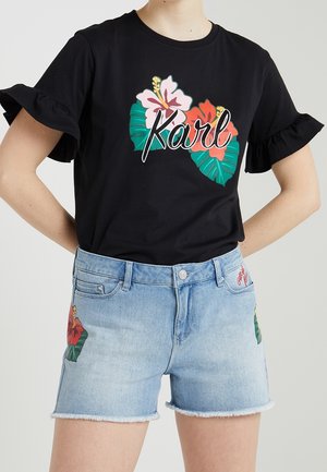 Black T-shirt with ruffled sleeves featuring colorful floral and leaf graphics, paired with light blue denim shorts with similar floral designs.