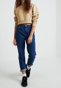Beige zkrácený svetr, volné modré džíny, ohrnuté manžety, černé tenisky, strukturovaný materiál a minimalistický design.