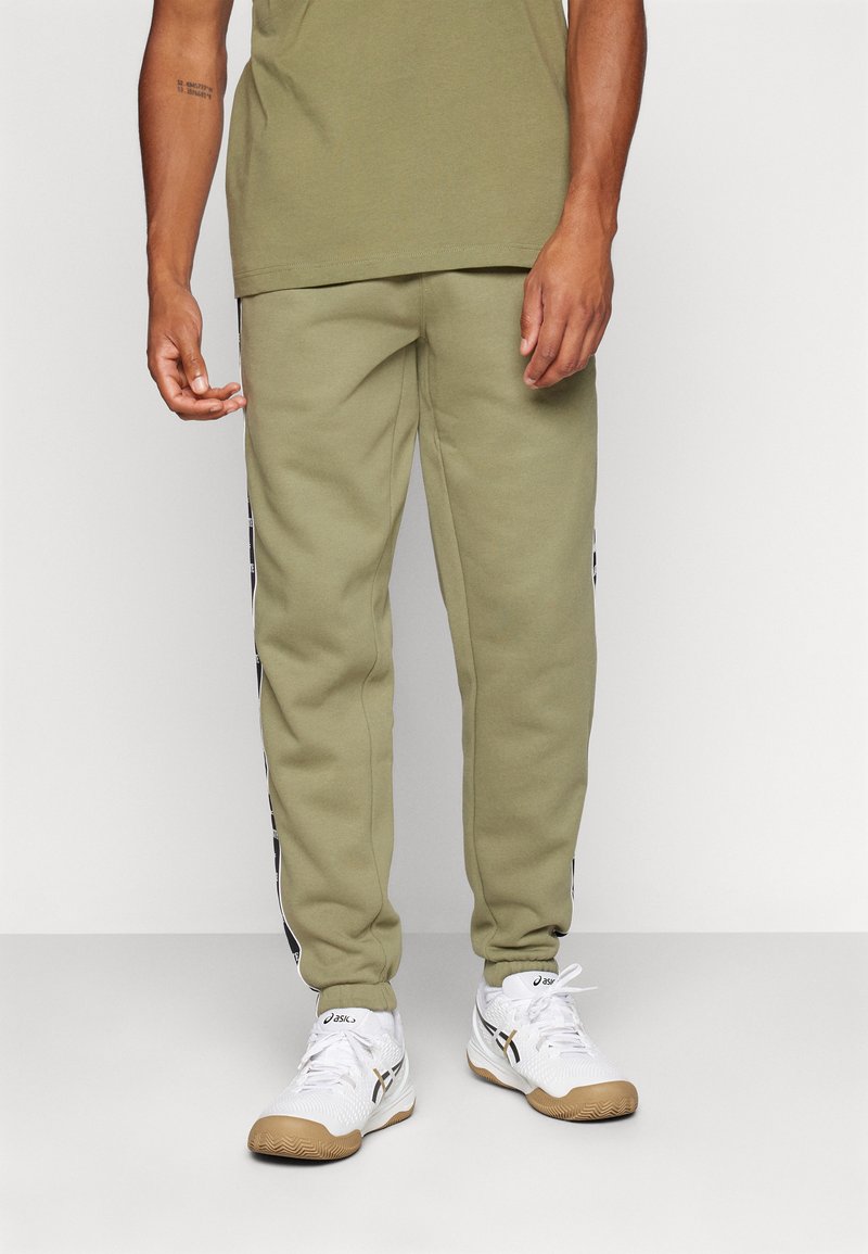 Joggers verde oliva hechos de un tejido suave con franjas laterales y puños. Combinados con zapatillas deportivas blancas con suela de goma.