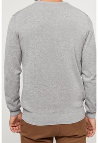 Sweat-shirt gris à manches longues avec poignets côtelés. Présente un col rond et une texture lisse. Porté avec un pantalon marron. Vue de dos.