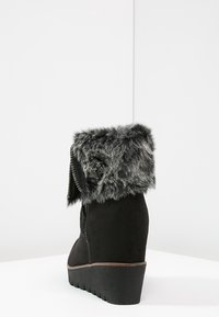 Černé semišové boty s límcem z umělé kožešiny, bočním zipem a klínovým podpatkem. Texturovaná látka a výrazný silueta. Čistý design, moderní vzhled.