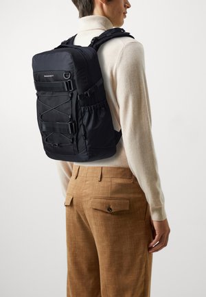 Black fabric backpack with adjustable straps and front bungee cords. Features a sleek rectangular shape and multiple pockets for storage.