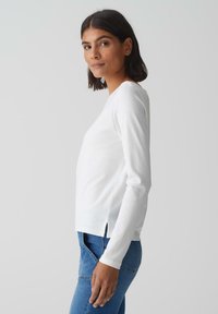 Witte langemouwen top met een ronde hals, zijsplitten en een gladde textuur, gecombineerd met blauwe denim jeans. Eenvoudig, passend ontwerp.
