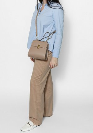 Donna che indossa una camicia azzurro chiaro, pantaloni beige a righe larghe, mocassini bianchi e porta una borsa a tracolla in pelle taupe con chiusura dorata.