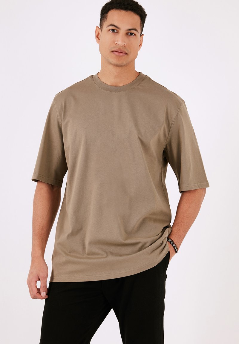 Camiseta de manga corta color caqui hecha de tejido ligero. Presenta un escote redondo y un corte relajado. Diseño minimalista sin patrones ni acentos.