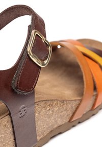 Sandalo in pelle marrone con fibbia dorata, caratterizzato da listini superiori multicolori e una suola in sughero testurizzata. Il plantare morbido è visibile.