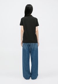 Črna polo majica s kratkimi rukavi v kombinaciji s širokimi modrimi kavbojkami, pogled od zadaj. Preprost dizajn, bombažni material, klasičen kroj.