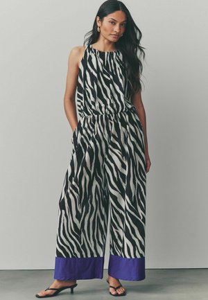 Ärmlös jumpsuit i svart och vit zebramönster, med en samlad halsringning, elastisk midja och lila kantdetaljer.