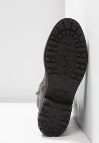 Grauer Stiefel mit einer strukturierten Gummisohle, die ein Zickzack-Profil aufweist, und einem Metallreißverschlussdetail an der Seite.