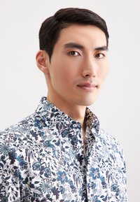 Camicia bianca con stampa floreale in blu e navy scuro, con colletto alla francese e motivi dettagliati su tutta la stoffa.