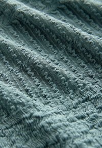 Tekstuuriga kangas muted teal värvuses, kus on kõrgenenud, lainelised jooned ja peened täpid. Pehme, kootud välimus, mis toob esile eristuvad sooned.