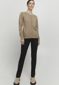Beige cardigan with a round neckline, button front, and ribbed cuffs, paired with black slim-fit pants and beige ankle boots.