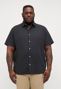 Chemise noire à manches courtes, à boutons, fabriquée en tissu léger, avec un col pointu et des boutons blancs, offrant une coupe décontractée.
