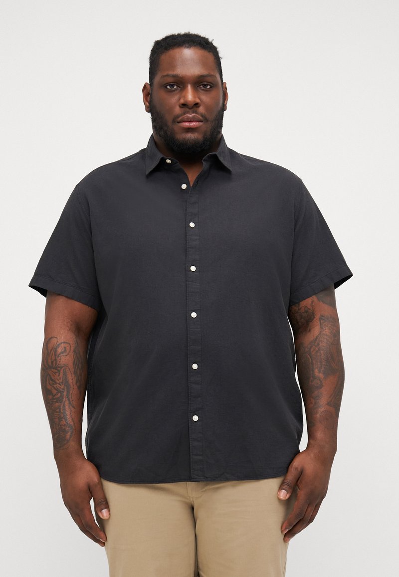Chemise noire à manches courtes, à boutons, fabriquée en tissu léger, avec un col pointu et des boutons blancs, offrant une coupe décontractée.