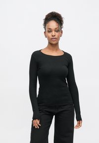 Schwarzes, geripptes Langarmshirt mit rundem Ausschnitt und figurbetontem Schnitt. Verfügt über schmale Bündchen, die über die Handgelenke hinausreichen.