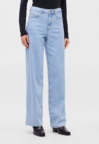 Ανοιχτό γαλάζιο τζιν παντελόνι σε σχέδιο φαρδιάς γραμμής, από τζιν ύφασμα, με ψηλή μέση, πέντε τσέπες και ραμμένες λεπτομέρειες. Φοριέται με μαύρες μπότες με τακούνι.