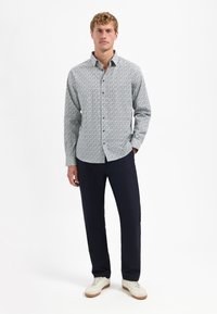 Wit overhemden met donkerblauw verspreid patroon, lange mouwen en kraag. Gecombineerd met donkere broeken en lichte sneakers.