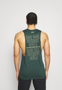 Top de tirantes verde sin mangas con un diseño holgado y espalda descubierta, y un texto en colores contrastantes en la parte posterior.