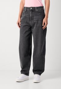 Black high-waisted jeans with a relaxed fit, five-pocket design, and visible stitching; worn with white sneakers.