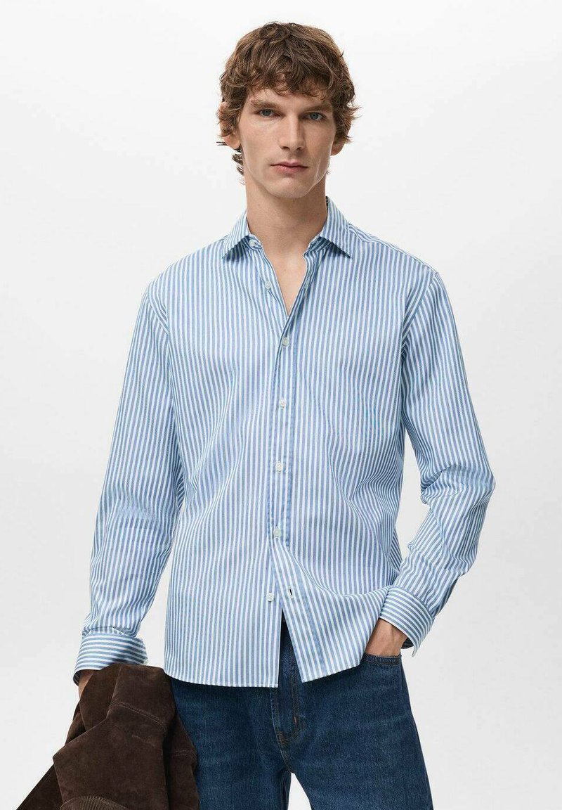 Camicia a righe azzurra chiaro e bianca con bottoni, colletto aperto e maniche lunghe, abbinata a jeans di denim scuro.
