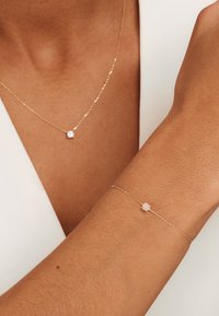 Collier et bracelet en chaîne dorée avec un petit centre en cristal transparent rond. Texture lisse et design délicat.