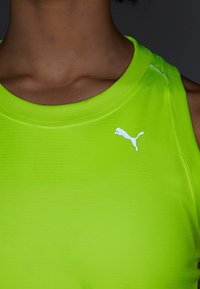 Limegrön ärmlös träningsskjorta med rund krage, med en texturerad tyg och en vit Puma-logotyp på bröstet.