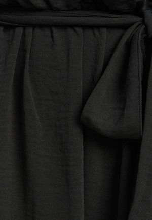 Zwart geweven stof met een zachte textuur, voorzien van een geraffineerde taille en een strikdetail voor sluiting. Inclusief een soepele, gedrapeerde uitstraling.