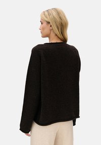 Brązowy sweter z dzianiny o luźnym kroju, okrągłym dekolcie, opuszczonych ramionach i teksturowanej tkaninie. Dół swetra ma lekko zaokrąglony kształt.