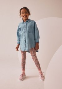 Denim skjortekjole med knapper foran, løs pasform og brystlomme, kombineret med blomstermønstrede leggings og pink sportssko med hvide såler.