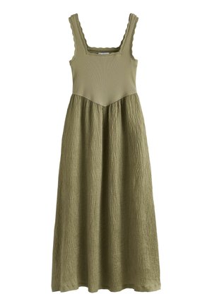 Rankovių neturinti alyvuogių žalia suknelė su siaurutėmis sijonėlėmis, kvadratine iškirpte, banguotomis petnešėlėmis ir tekstūruota, laisvai krintančia suknia, siekiančia vidurio blauzdos.