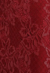 Tissu en dentelle rouge avec des motifs floraux, une surface texturée et une qualité semi-transparente, superposé à un fond unicolore et lisse.