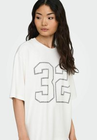 Maglietta oversize bianca con grafica nera a pois "32" sul davanti. Tessuto morbido, collo tondo, maniche corte, vestibilità rilassata.