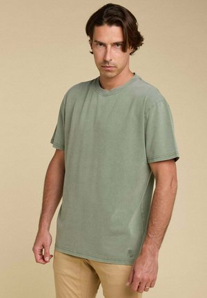 T-shirt en coton olive avec un col rond et des manches courtes ; coupe décontractée ; présente un logo discret sur le côté inférieur.