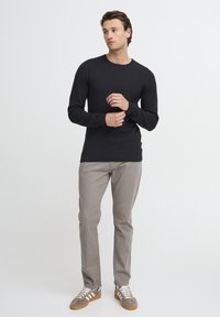 Camisetă albastră texturată cu mânecă lungă, cu decolteu rotund, asortată cu pantaloni gri deschis și adidași din suede gri cu șireturi albe.