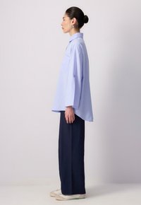 Cămașă supradimensionată cu dungi albastre deschise, cu guler, mâneci lungi și un buzunar frontal, asortată cu pantaloni largi negri și adidași albi.