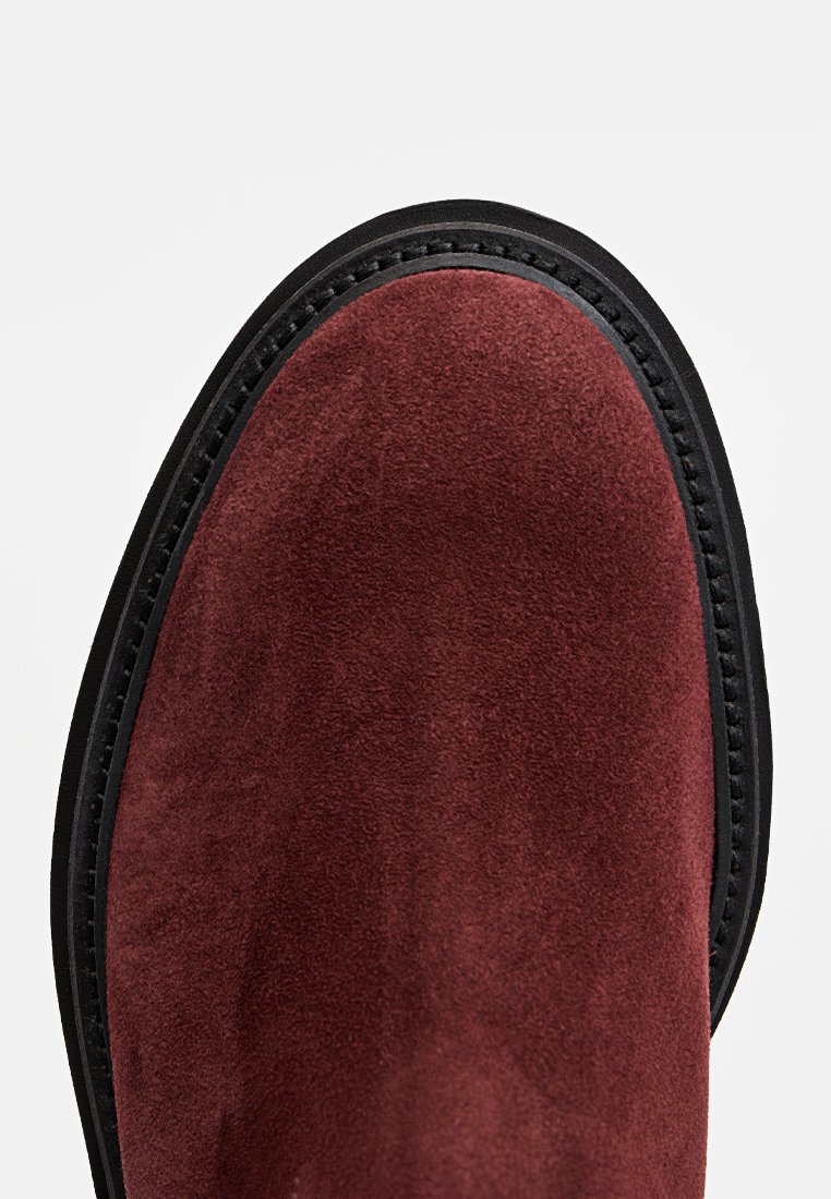 Bordeauxfarbene Wildleder-Stiefelette mit runder Zehenpartie, schwarzer Sohle und kontrastierendem Nähen entlang der Kante für zusätzliche Details.