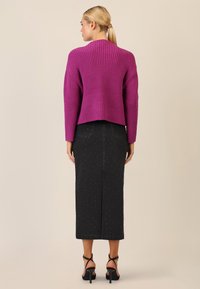 Maglione corto viola a coste con retro corto, abbinato a una lunga gonna di jeans nera con borchie e tacchi neri con cinturini.