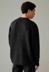 Schwarzer Strickpullover mit einem lockeren, strukturierten Design, der einen Rundhalsausschnitt und einen gerippten Saum hat. Kombiniert mit dunklen Jeans.