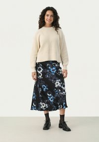 Beige stickad tröja med rund halsringning, i kombination med en svart blommig midikjol med blå och vita mönster. Svarta snörskor.