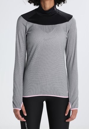 Femme portant un haut de sport gris et noir à manches longues et col montant avec des trous pour les pouces, et des leggings noirs.